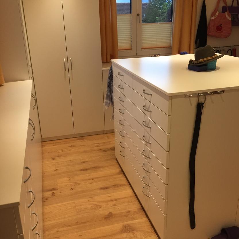 Begehbare Ankleide mit weißem Kleiderschrank und Schubladenelement in der Mitte des Raumes