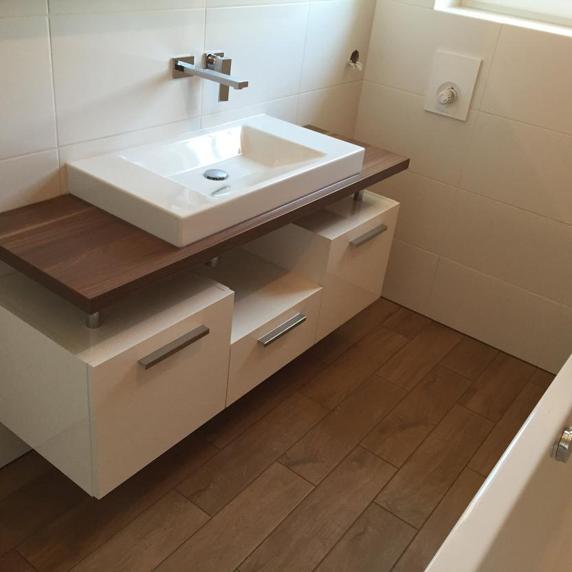 Modernes Badezimmermöbel mit weißem Unterschrank und Holzplatte, darauf eine rechte