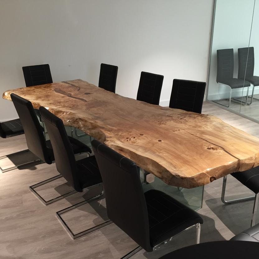 Rustikaler Holztisch auf Glasbeinen, umgeben von schwarzen Lederstühlen