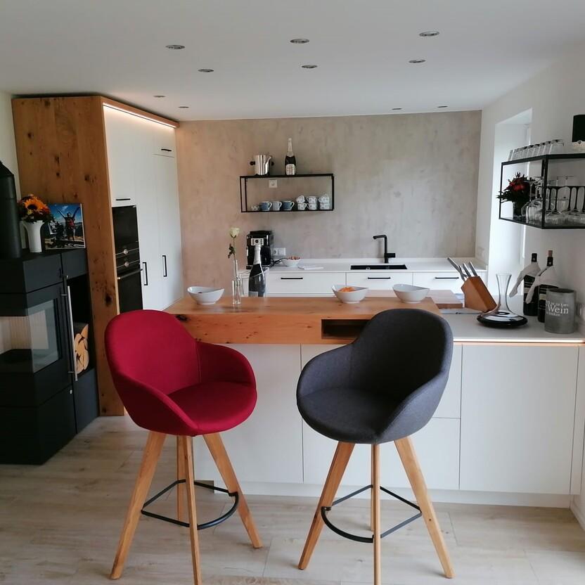 Moderne Küchenmöbel mit weißer Front, Eichenholz-Elementen und gemütlicher Barlösung im offenen Wohnbereich Küchenmöbel in Weiß mit Holzakzenten, Bartheke und Wandverkleidung in Betonoptik in heller Wohnküche