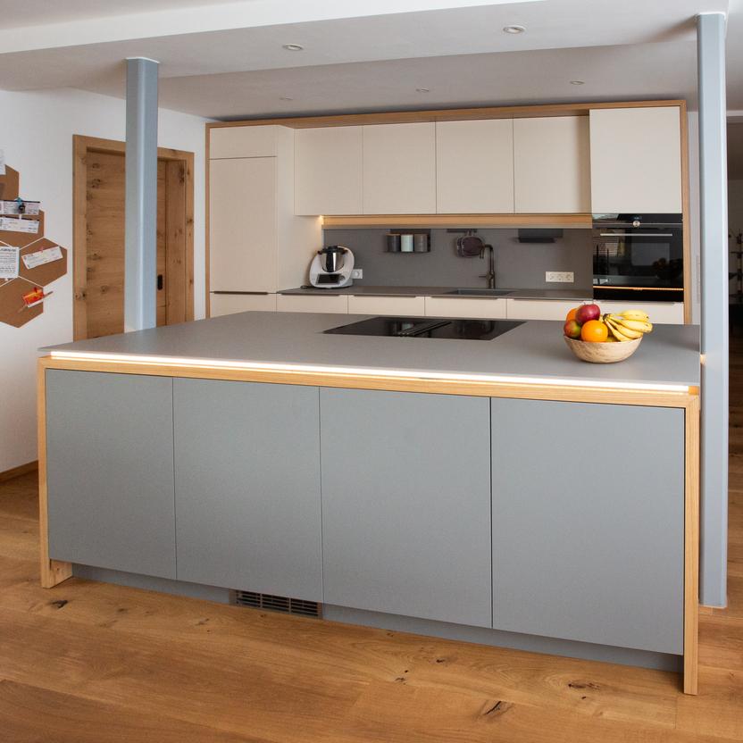 Küchenmöbel in Hellgrau mit Kochinsel, integrierter Beleuchtung und grifflosen Fronten in offener Wohnküche