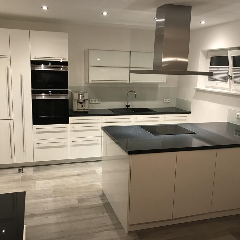 Weißer Küchenblock mit dunkler Arbeitsplatte, Einbaugeräten und Insel in einem hellen Raum