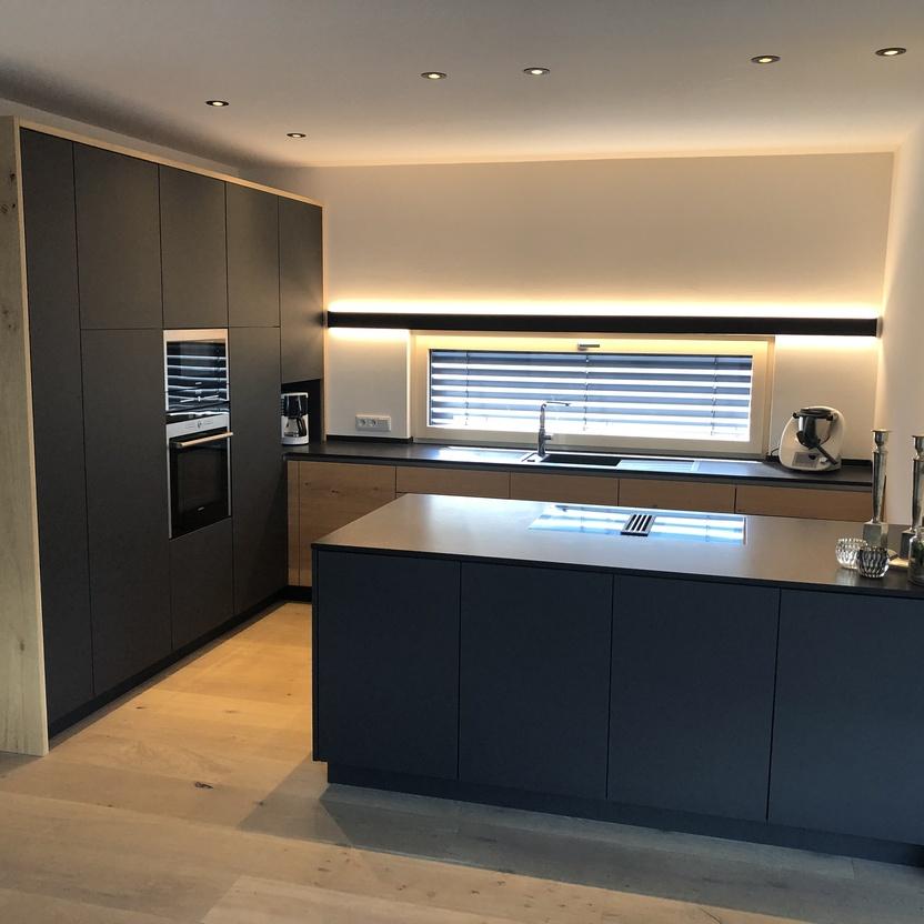 Küchenmöbel in Anthrazit mit Holzdetails, Kochinsel und indirekter Beleuchtung in moderner Wohnküche