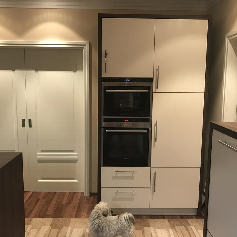 Küchenmöbel mit Hochschrank in Creme mit Einbaugeräten und Holzdetails in einem warm gestalteten Küchenraum