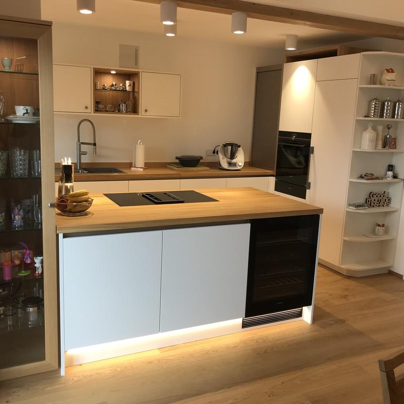 Küchenmöbel mit Kochinsel, Holzarbeitsplatte, beleuchtetem Sockel und offenem Regal in heller, moderner Küche