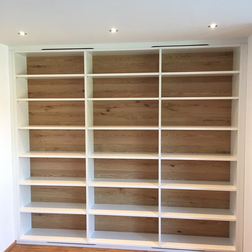 Leeres weißes Bücherregal mit Eichenrückwand in einem hellen Raum mit Parkettboden.