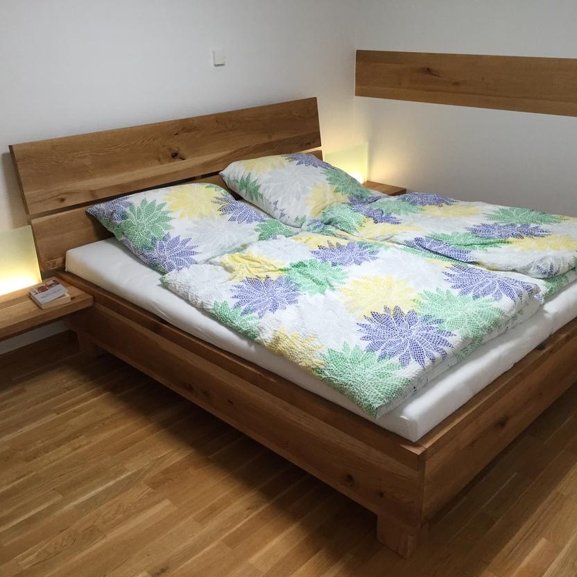 Massivholzbett aus Eiche mit integriertem Nachttisch und floralem Bettbezug im Schlafzimmer.