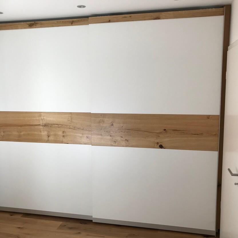 Moderner Schiebetürenschrank in Weiß mit Holzstreifen aus Eiche und minimalistischem Design.