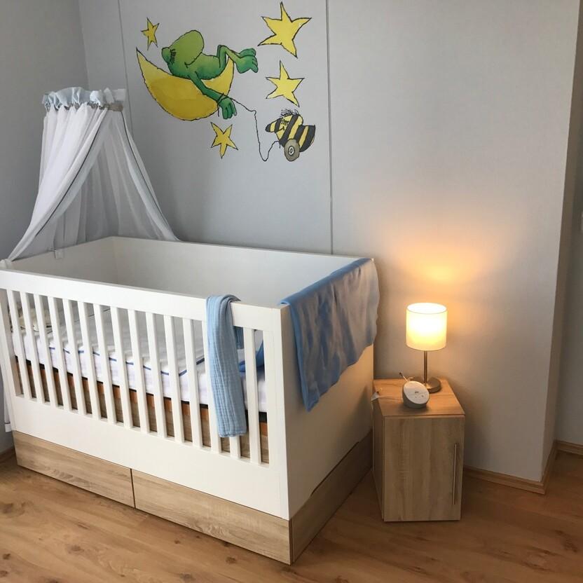 Modernes Babybett aus Holz mit Himmel, Wandmalerei und warmer Beleuchtung im Kinderzimmer.