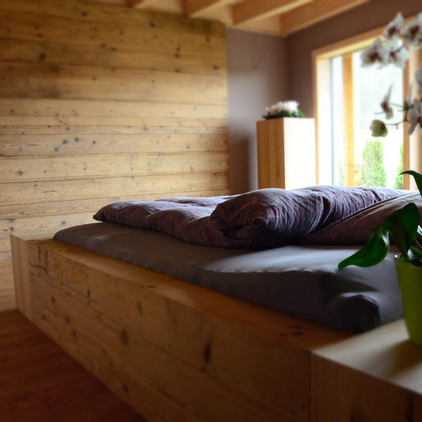 Rustikales Schlafzimmer mit Holzwand, massivem Holzbett und Blick auf den Garten durch große Fenster.