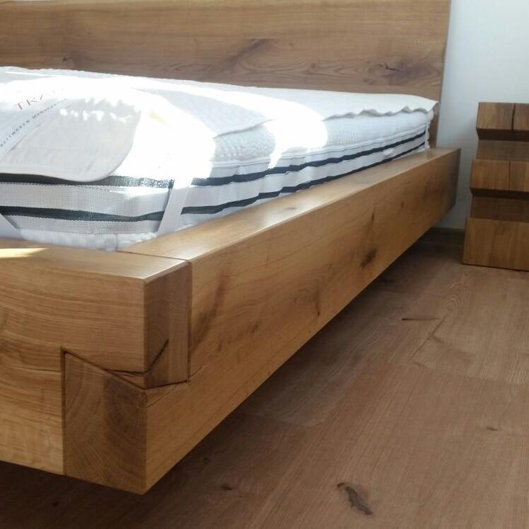 Massivholzbett mit weißer Matratze und gestreiften Kissen neben einem blockförmigen Nachttisch.