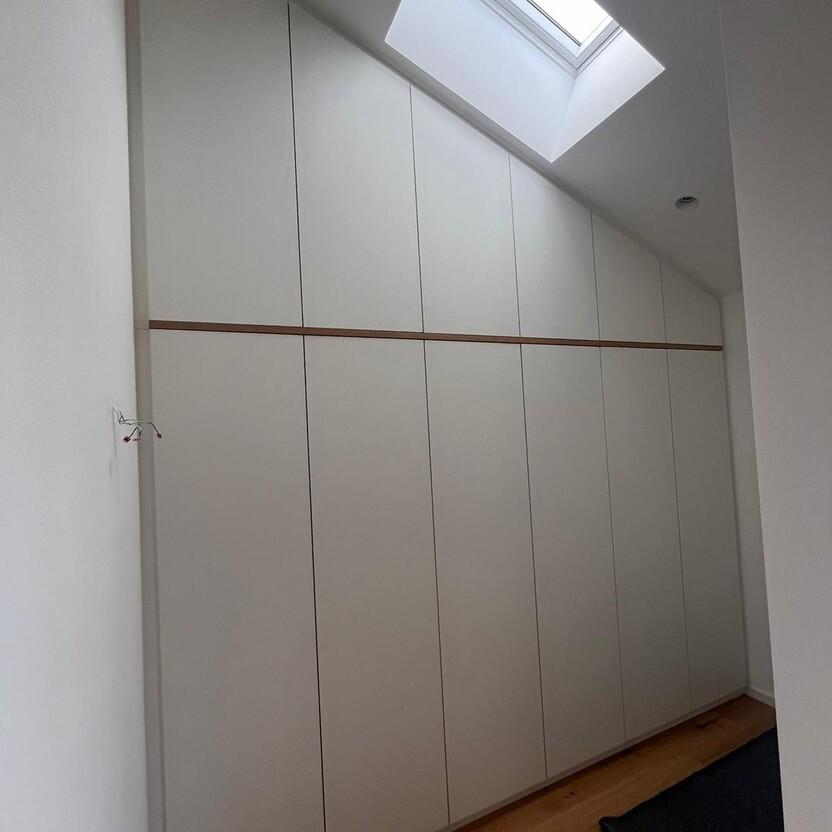 Individuell gefertigter Einbauschrank in Weiß mit Holzlinie, passgenau unter Dachschräge montiert.