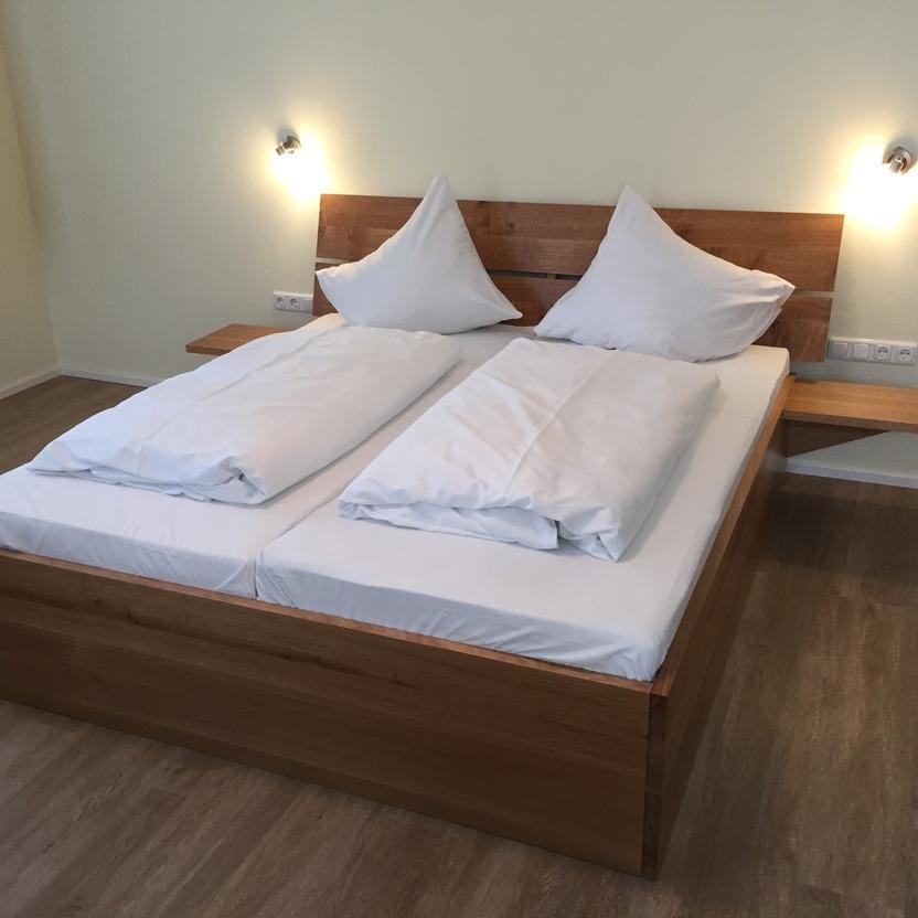 Handgefertigtes Doppelbett aus Massivholz mit schlichtem Kopfteil und integrierten Nachttischen.