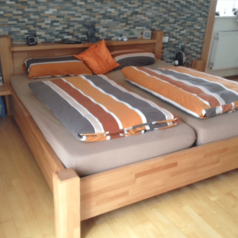 Gemütliches Doppelbett aus massiver Buche mit orangebrauner Bettwäsche.