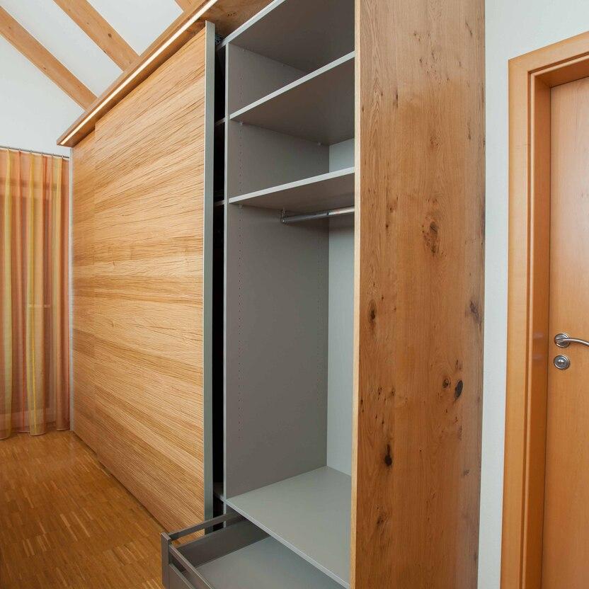 Detailaufnahme eines Eichenholz-Schiebetürenschranks mit offenen Regalfächern und Schublade.