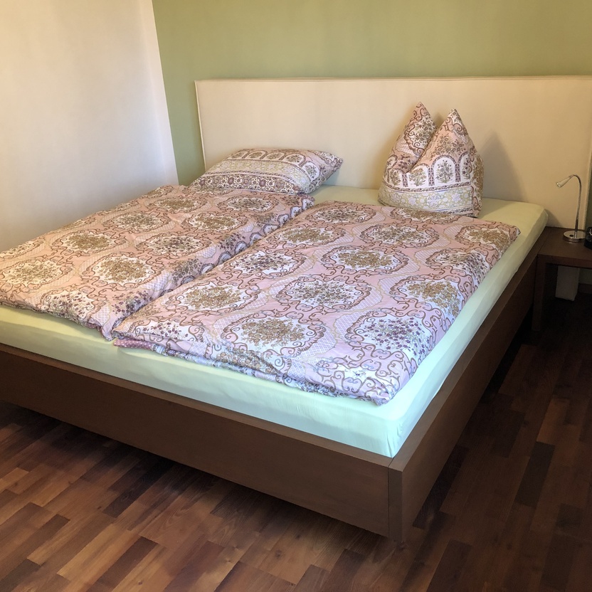 Modernes Doppelbett aus Akazienholz mit gepolstertem Kopfteil und passendem Nachttisch.