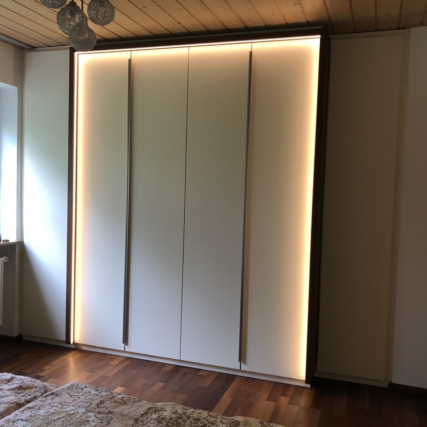 Heller Einbauschrank mit integrierter LED-Beleuchtung und glatten weißen Fronten im Schlafzimmer.