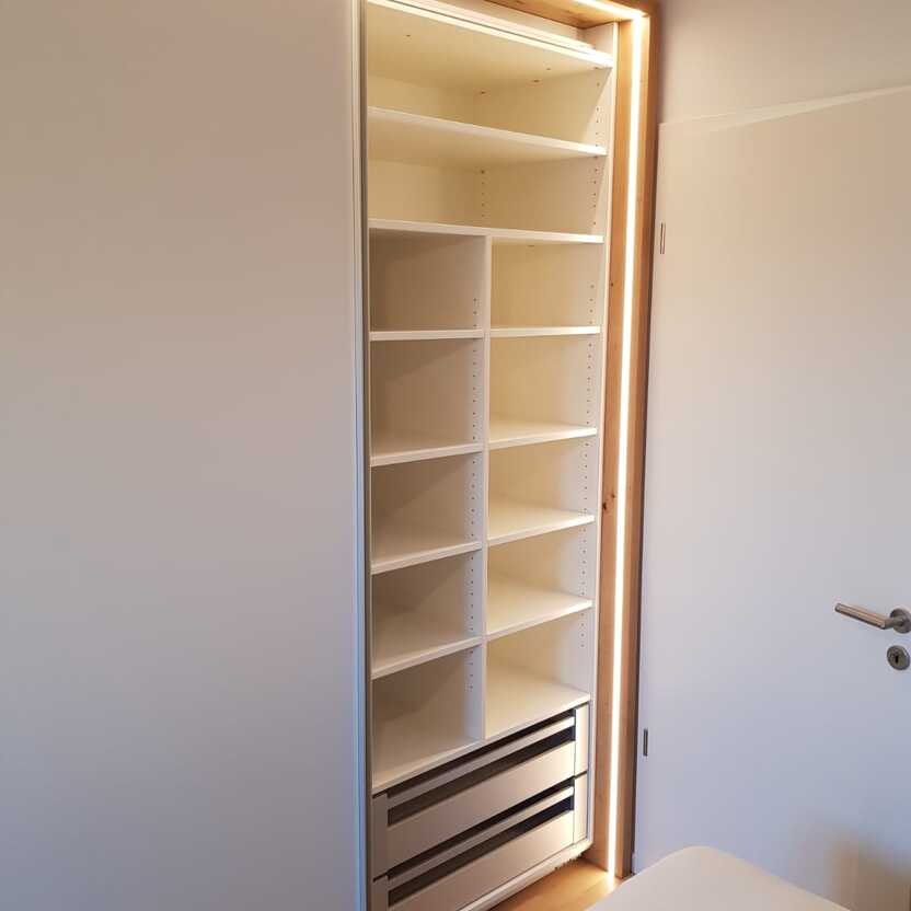 Maßgefertigter Kleiderschrank mit weißen Fronten und LED-Beleuchtung, innen mit Regalen und Schubladen.