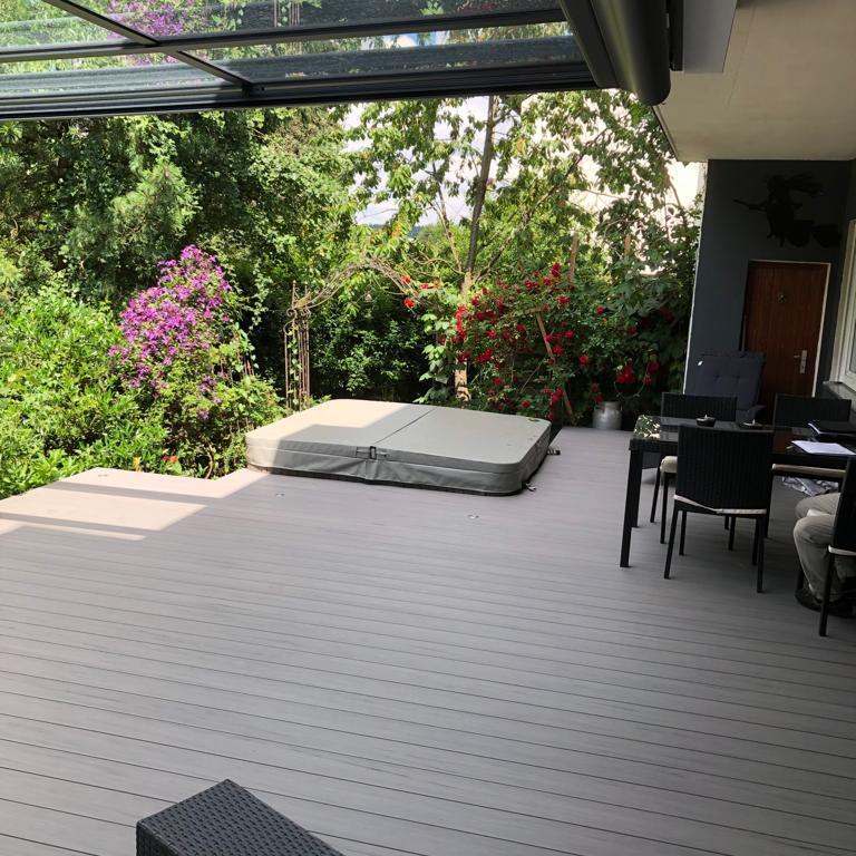 Blick von einer modernen Terrasse mit Loungemöbeln auf blühende Sträucher und Bäume.