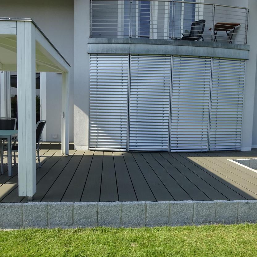 Moderne Hausaußenterrasse mit Essbereich und Jalousien. Eine Außenterrasse mit einem Essbereich unter einem Pavillon und geschlossenen Jalousien an der Wand.