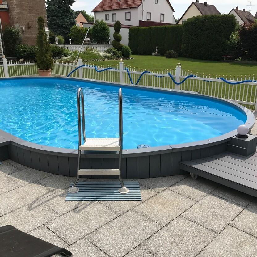 Garten mit einem runden Aufstellpool und Terrassendeck. Ein runder blauer Pool mit Leiter und umgebendem grauen Deck in einem gepflegten Garten mit Zaun.