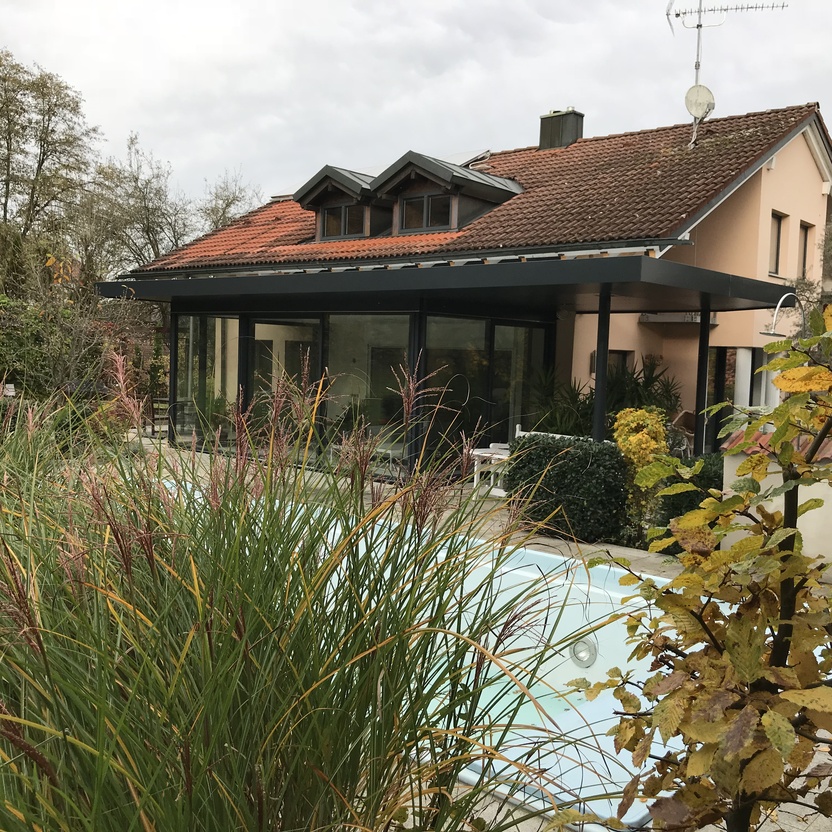 Moderner Wintergarten mit Flachdach und Glasfronten an einem Einfamilienhaus mit Garten und Pool