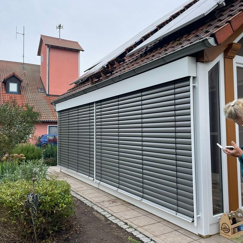 Wintergarten mit außenliegendem Sonnenschutz in Form von Lamellenjalousien und weißem Rahmen am Wohnhaus