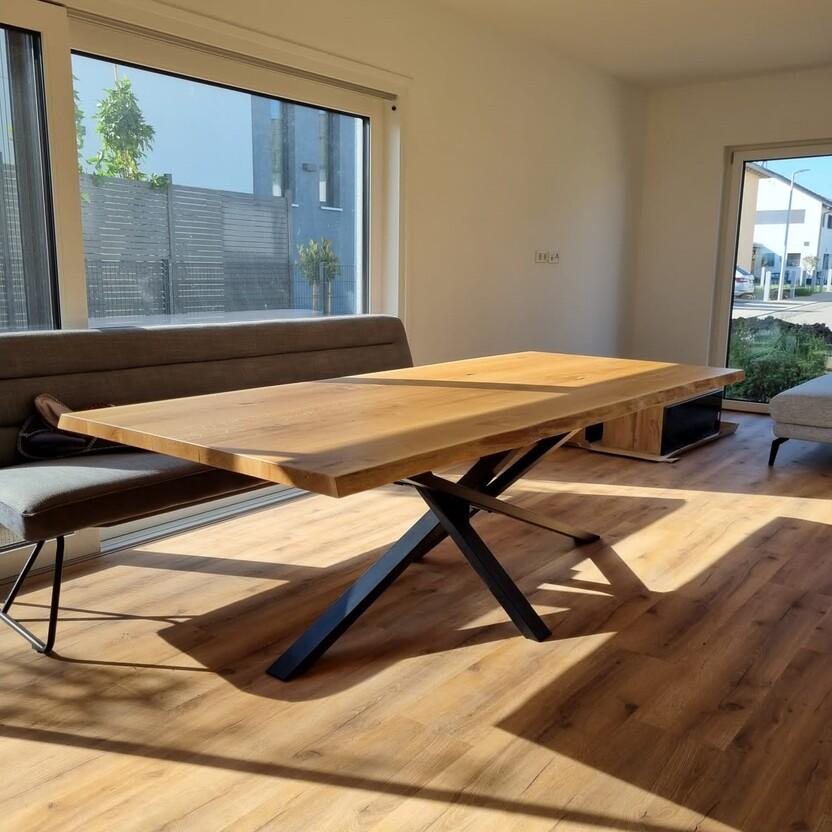 Großer Eichentisch mit markantem Metallgestell in einem sonnigen Raum mit Blick nach draußen.