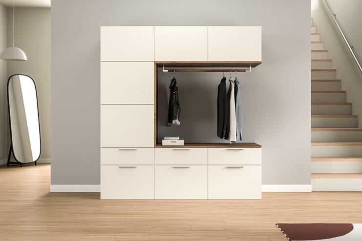 Ein maßgefertigter Garderobenschrank in Cremeweiß mit Holzakzenten bietet eine elegante Aufbewahrungslösung im Eingangsbereich, inklusive einer Kleiderstange und Stauraum.